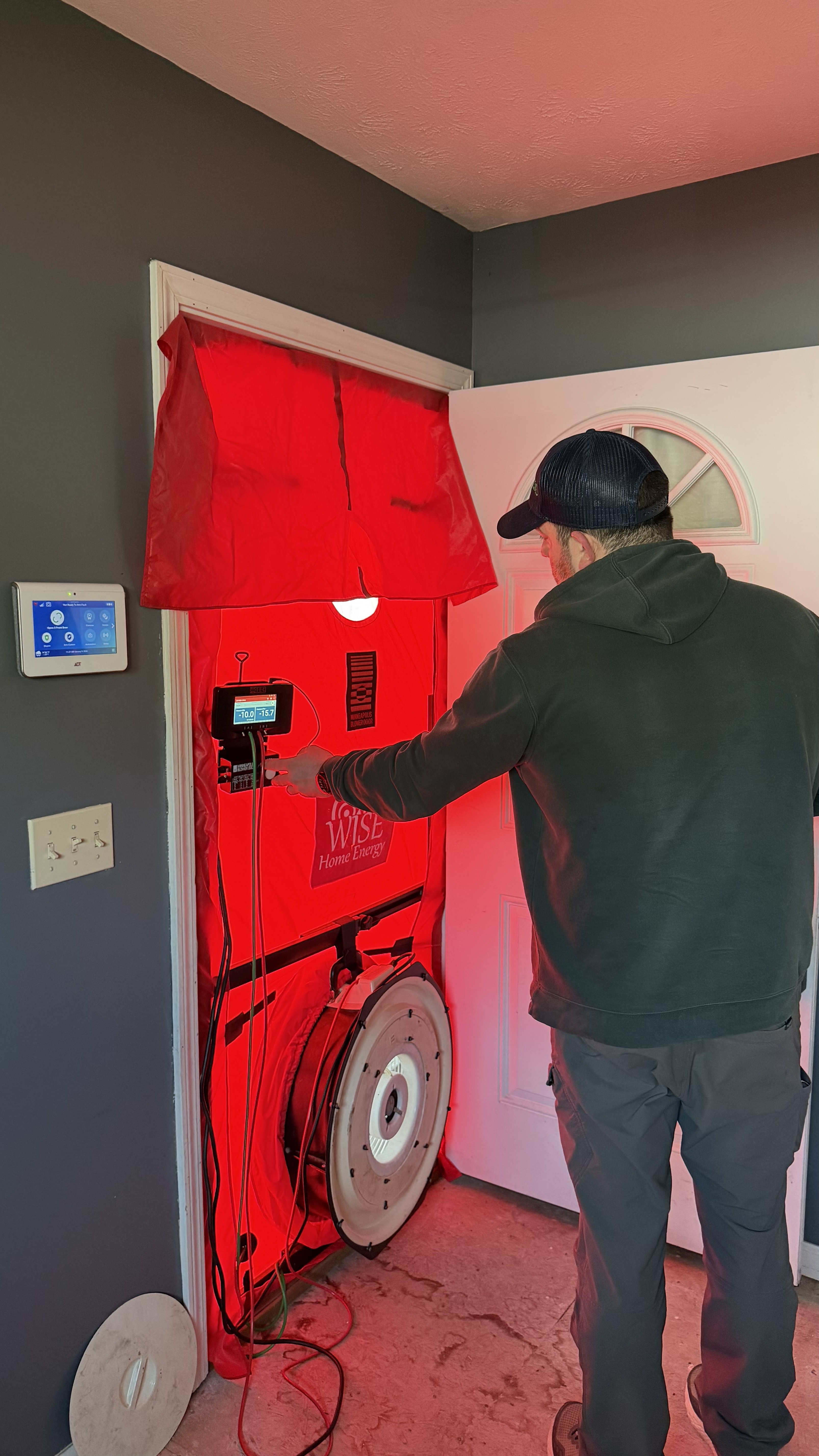 A Wise Home Energy building analyst standing in front of a blower door while performing a test on a home.